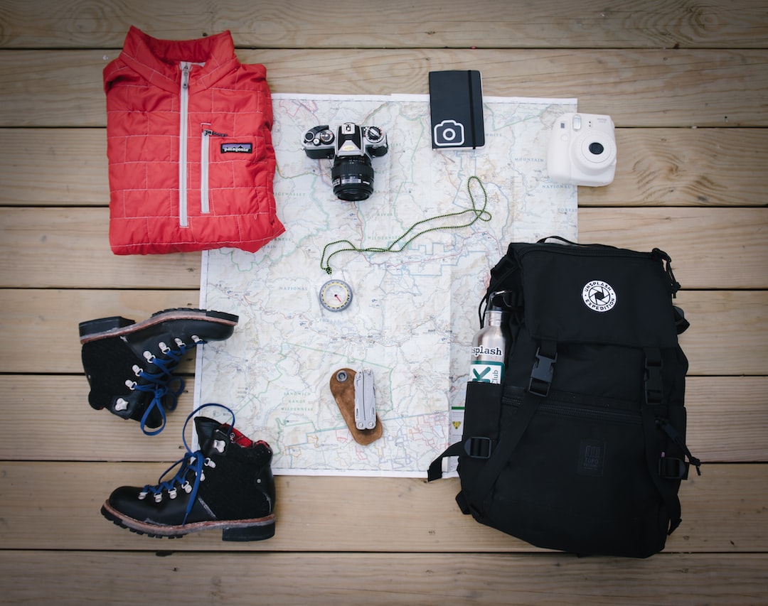 An image of a vibrant mountaintop with a clear blue sky, showcasing a selection of top-tier adventure gear, including sturdy hiking boots, weatherproof tents, reliable backpacks, and high-performance climbing equipment