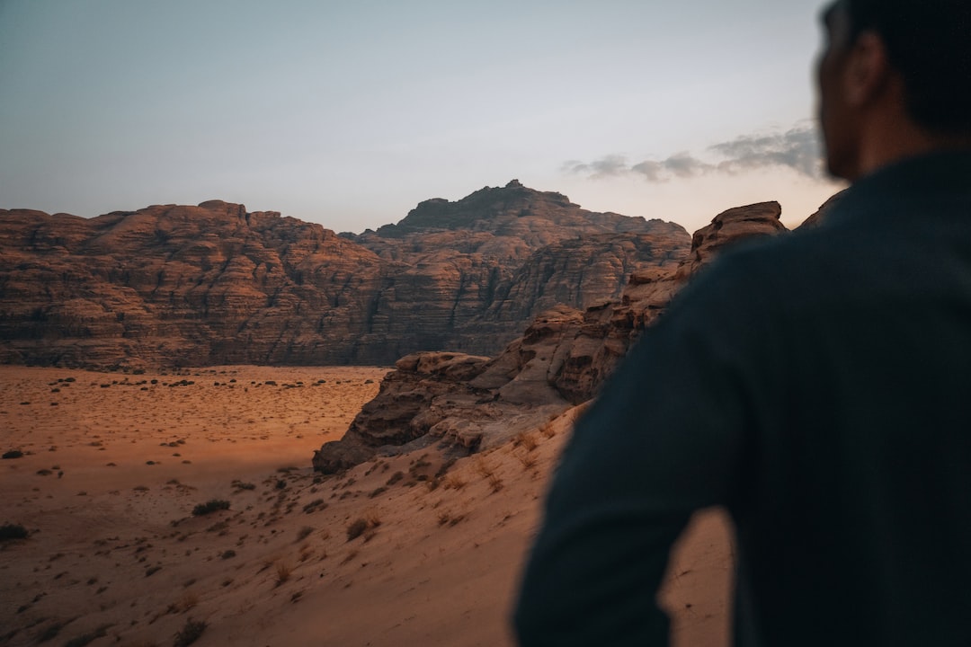 An image capturing a lone hiker, bathed in golden sunlight, conquering a rugged mountain peak, their determined expression mirroring the breathtaking views of vast valleys and towering peaks stretching into the distance