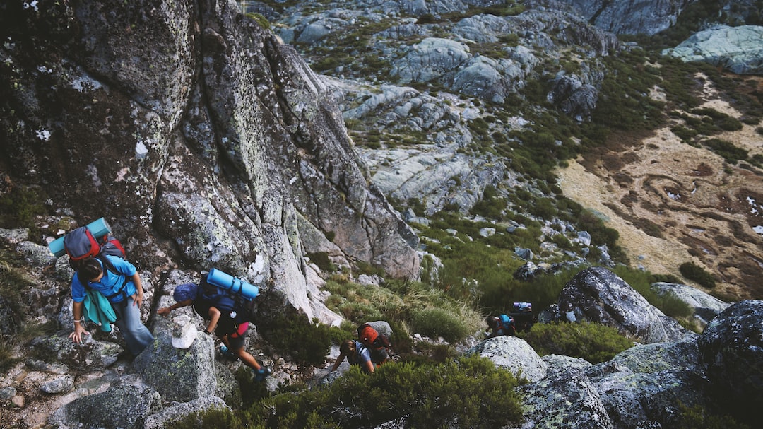 An image showcasing a pair of sturdy hiking boots, laced tightly, with mud-caked soles and a backdrop of a picturesque, rugged trail winding through lush green forests and towering mountains