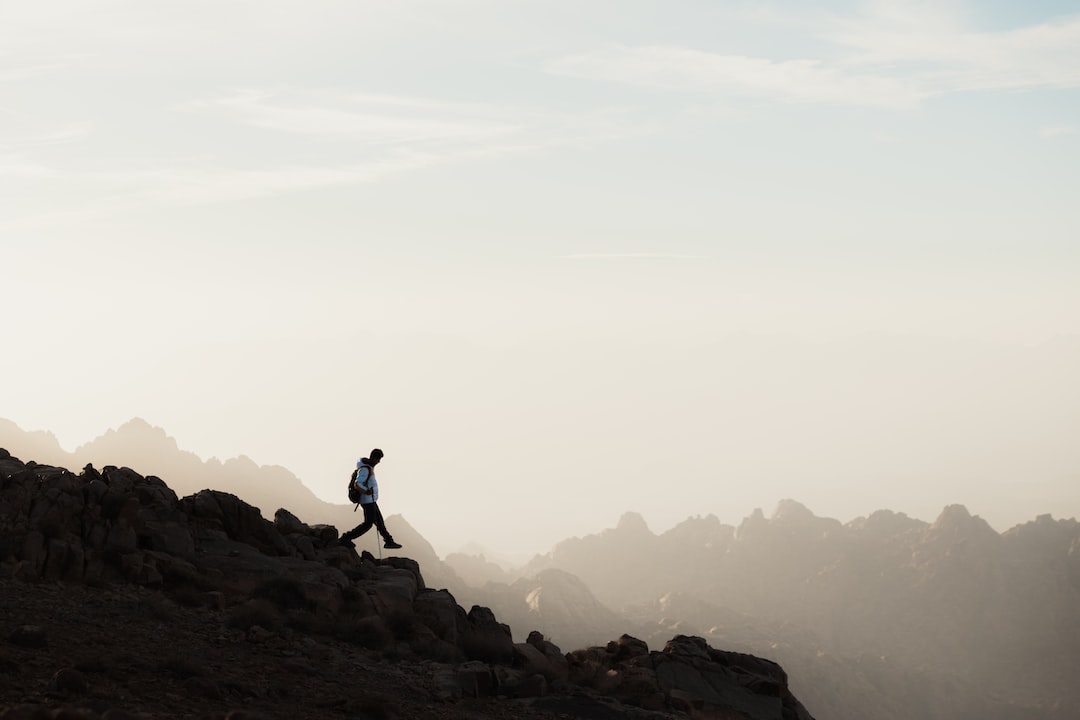 the breathtaking beauty of Trilha Da Pedra Grande: A panoramic view of lush green hills stretching into the horizon, with rugged trails winding through the landscape and a hiker standing at the edge, soaking in the awe-inspiring vista