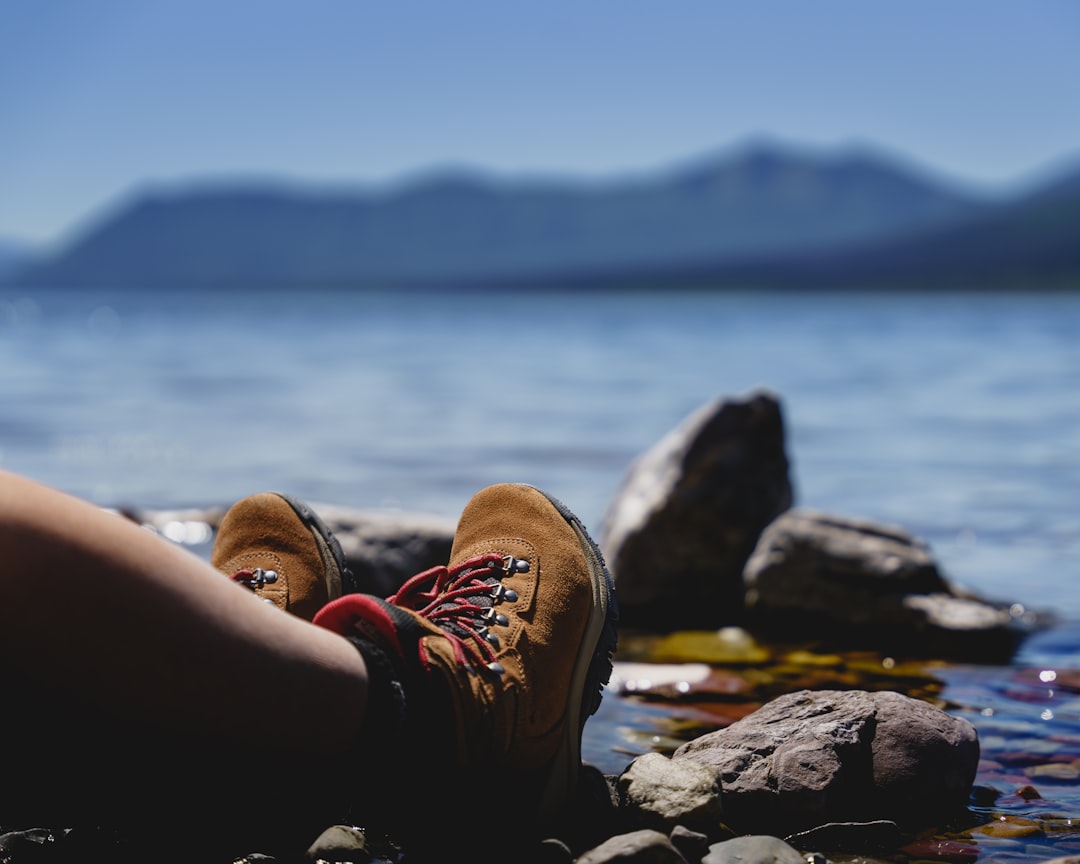 Create an image showcasing a pair of sturdy women's hiking boots, adorned with rugged yet feminine design elements, standing proudly on a moss-covered trail, surrounded by lush greenery and majestic mountains in the background